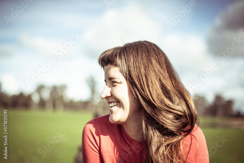 Girl with fringe laughs in sunlight out on green farm land in spring