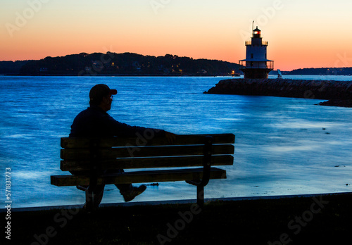 Silhouetted man watches pre-dawn glow near coast of Maine lighthouse