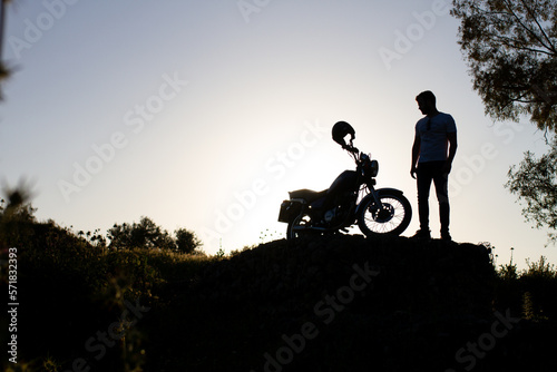 backlight of a man watching his beautiful motorcycle on a rock in the photo