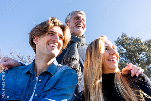Low angle of young man in denim jacket spending free time with mature mother and father in park having family time smiling