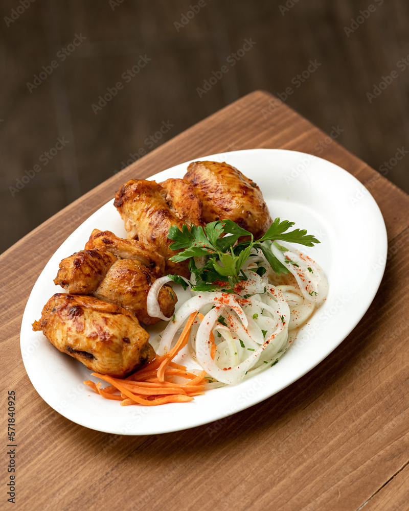 Few pieces of fried meat garnished with fresh vegetables. Shashlik with carrots and onions garnished with parsley on white plate. Roasted chicken. Soft focus. Copy space. Top view. 