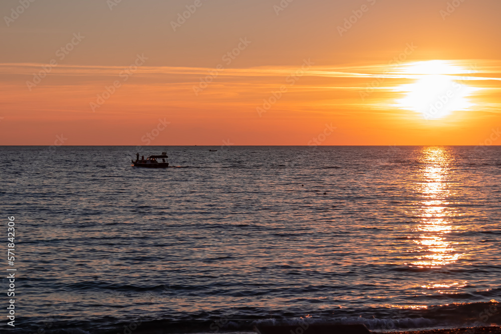 Small fishermen boat with scenic sunset view from Sveti Stefan at Adriatic Mediterranean Sea, Budva Riviera, Montenegro, Europe. Reflection of sun beams on water surface. Summer vacation atmosphere