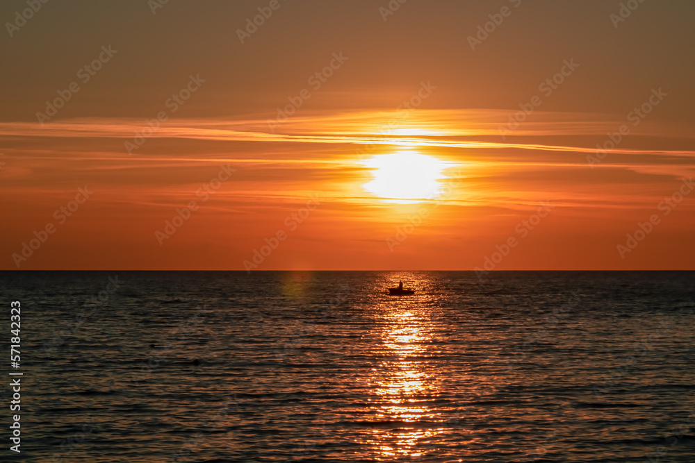 Small fishermen boat with scenic sunset view from Sveti Stefan at Adriatic Mediterranean Sea, Budva Riviera, Montenegro, Europe. Reflection of sun beams on water surface. Summer vacation atmosphere