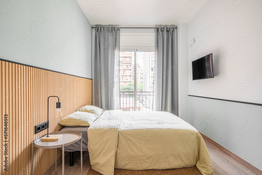 Bedroom with large bed for two persons against backdrop of glass sliding door with access to small balcony. Curtains on door protect from bright sun during day. On wall is TV for watching movies. Bedroom with large bed for two persons against backdrop of glass sliding door with access to small balcony. Curtains on door protect from bright sun during day. On wall is TV for watching movies.