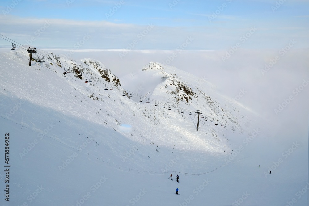 Little silhouettes of skier on slope of Kasprowy Wierch Peak in Tatras Mountains, famous place in Tatras with cable railway. Poland. Dramatic clouds scenery.