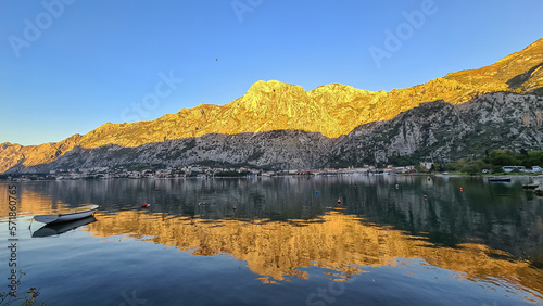 Panoramic view of bay of Kotor at sunset in summer, Adriatic Mediterranean Sea, Montenegro, Balkans, Europe. Fjord winding along coastal towns. First sunbeams on Lovcen mountains. Water reflection