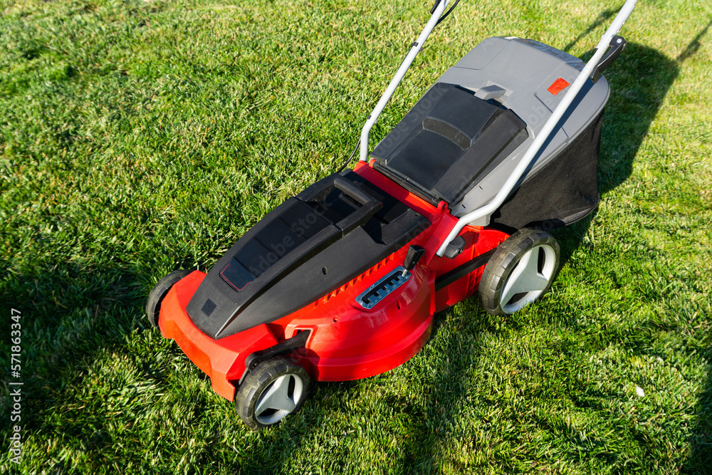 Fototapeta premium Electric Lawn mower on a green meadow. Garden equipment