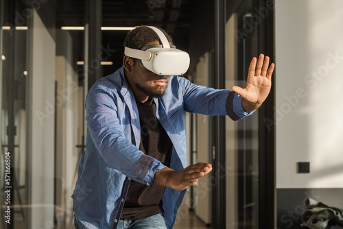 Black man in vr headset exploring metaverse world, touching virtual reality subjects. Abstract cyber world in office