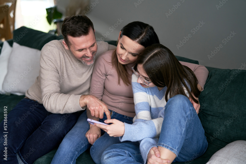 Caucasian family have fun together with mobile phone while relaxing at the sofa Caucasian family have fun together with mobile phone while relaxing at the sofa