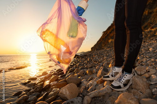 Coastal cleaning. Activist puts a picked-up plastic bottle in a garbage bag, close-up. The concept of cleanup from environmental pollution and Earth Day