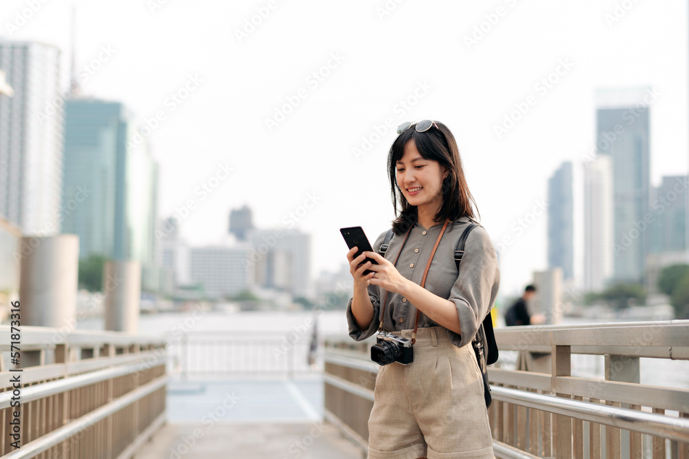 Young Asian woman backpack traveler using mobile phone in express boat pier on Chao Phraya River in Bangkok. Young Asian woman backpack traveler using mobile phone in express boat pier on Chao Phraya River in Bangkok.