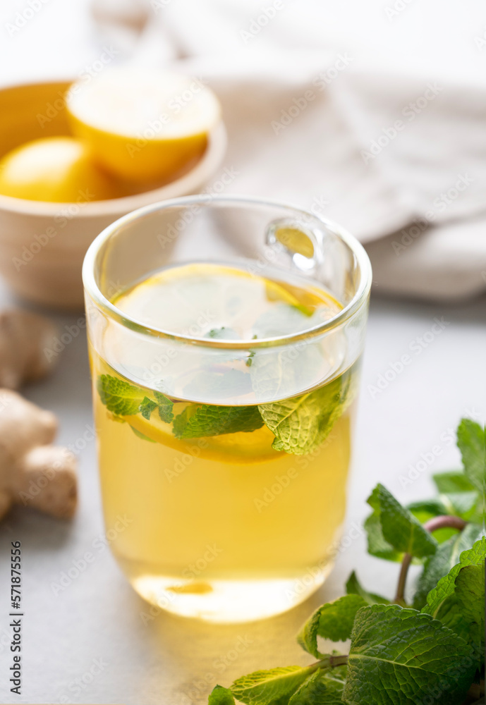 A glass of tea with fresh lemon, mint and ginger on a light background with morning light close up. A glass of tea with fresh lemon, mint and ginger on a light background with morning light close up.