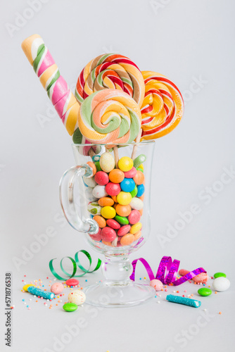 Colorful candies in cup on table on light background background. Large swirled lollipops. Creative concept of a jar full of delicious sweets from the candy store