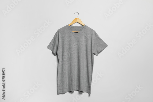 Hanger with grey t-shirt on light wall. Mockup for design