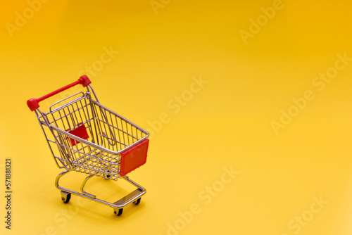 An empty mini supermarket cart on a yellow background.