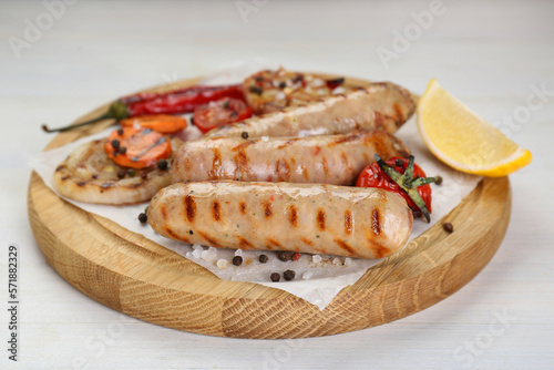 Tasty grilled sausages with vegetables, lemon and spices on white wooden table, closeup