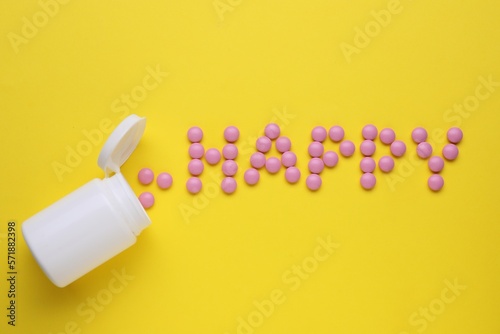 Word Happy made of pink antidepressants and medical bottle on yellow background  flat lay