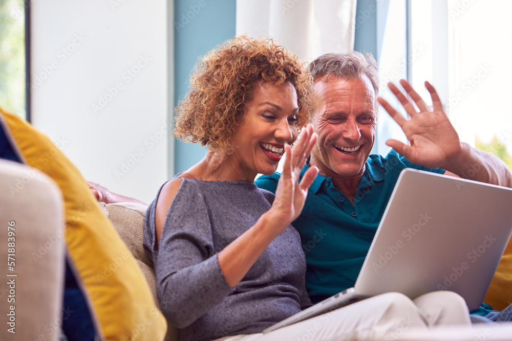 Senior Retired Couple Sitting On Sofa At Home Making Video Call On Laptop