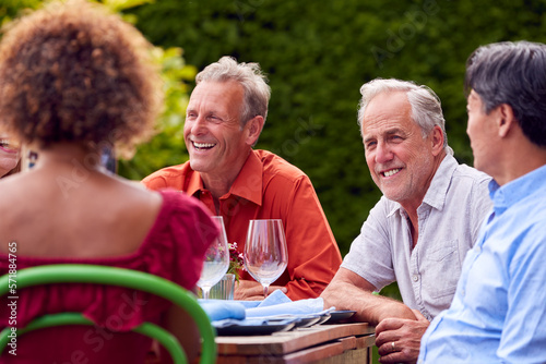 Canvas Print Group Of Mature Friends Talking Around Table At Summer Dinner Party In Garden At