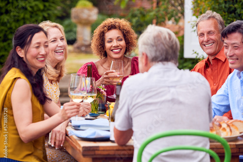 Group Of Mature Friends Talking Around Table At Summer Dinner Party In Garden At Home