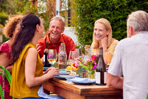 Group Of Mature Friends Talking Around Table At Summer Dinner Party In Garden At Home