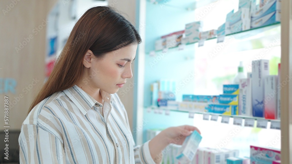 Beautiful young asian woman standing between shelves looking and shopping for medicine supplements products at pharmacy