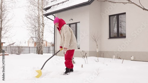 A girl cleans snow near the house. Consequences of snowfall