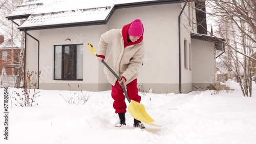 A girl cleans snow near the house. Consequences of snowfall