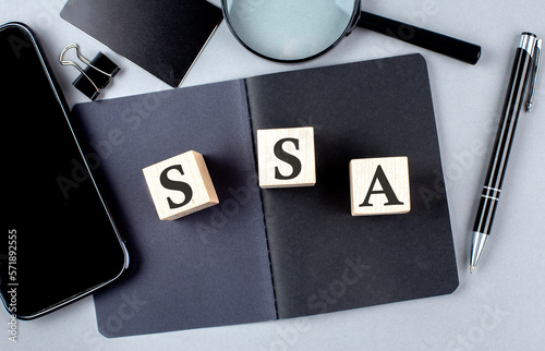 Word SSA on wooden block on black notebook with smartpone, credit card and magnifier photo