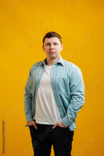 Portrait of handsome european man in shirt looking at camera standing on yellow studio background