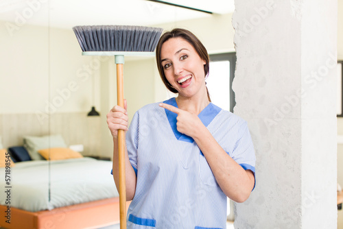 young pretty woman smiling cheerfully, feeling happy and pointing to the side. housekeeper concept