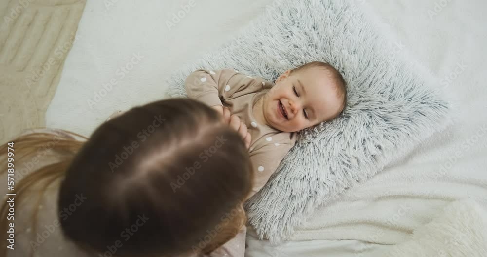 Top down view of mother playing with baby daughter on the bed, mom tickling her child Top down view of mother playing with baby daughter on the bed, mom tickling her child