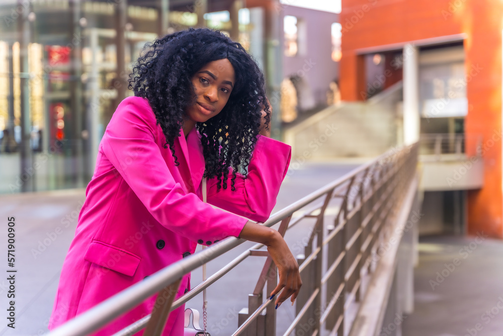 African American young woman in the city, portrait of a young woman in a pink jacket leaning on a railing
