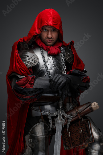 Shot of dark knight dressed in steel armor and red robe against gray background.