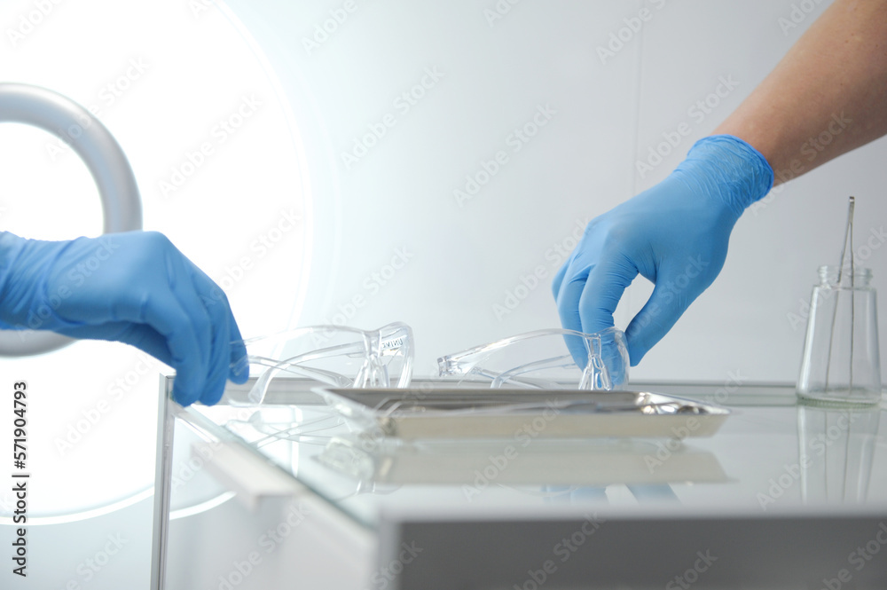 doctor nurse at same time put plastic transparent glasses on glass table with instruments for operations stomatology hospital hospital blue gloves sterile protective glasses close-up modern clinic doctor nurse at same time put plastic transparent glasses on glass table with instruments for operations stomatology hospital hospital blue gloves sterile protective glasses close-up modern clinic