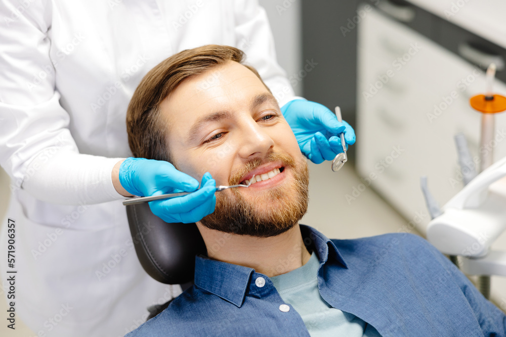 Portrait of happy man sitting at dentist chair in modern clinic and smiling. Patient enjoying dental treatment with professional stomatolog Portrait of happy man sitting at dentist chair in modern clinic and smiling. Patient enjoying dental treatment with professional stomatolog