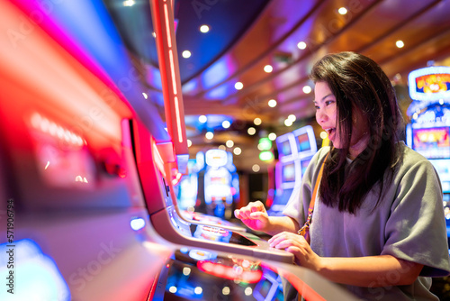 exited asia female woman slot machine gambling cheerful smile hand pressing bet button in casino club entertainment concept,exited asian woman hand play slot machine in casino hotel