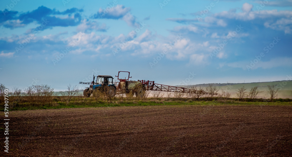 Obraz premium a tractor with a fertilizer sprayer trailer, preparing the land for crops and a beautiful sky in spring
