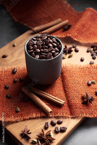 Coffee cup with roasted beans with two cinnamon stickson on black ceramic plate photo