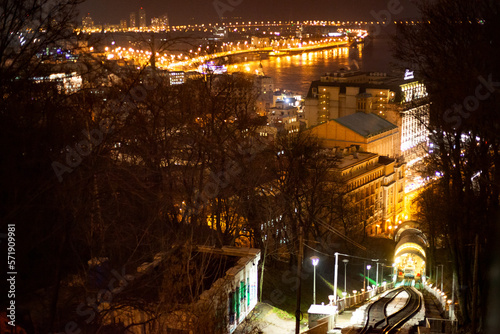 Nighttime Kyiv. Capital of Ukraine. Sight. View from the funicular to the embankment of the Dnieper River. The evening is dark, the lights are on. Street panorama