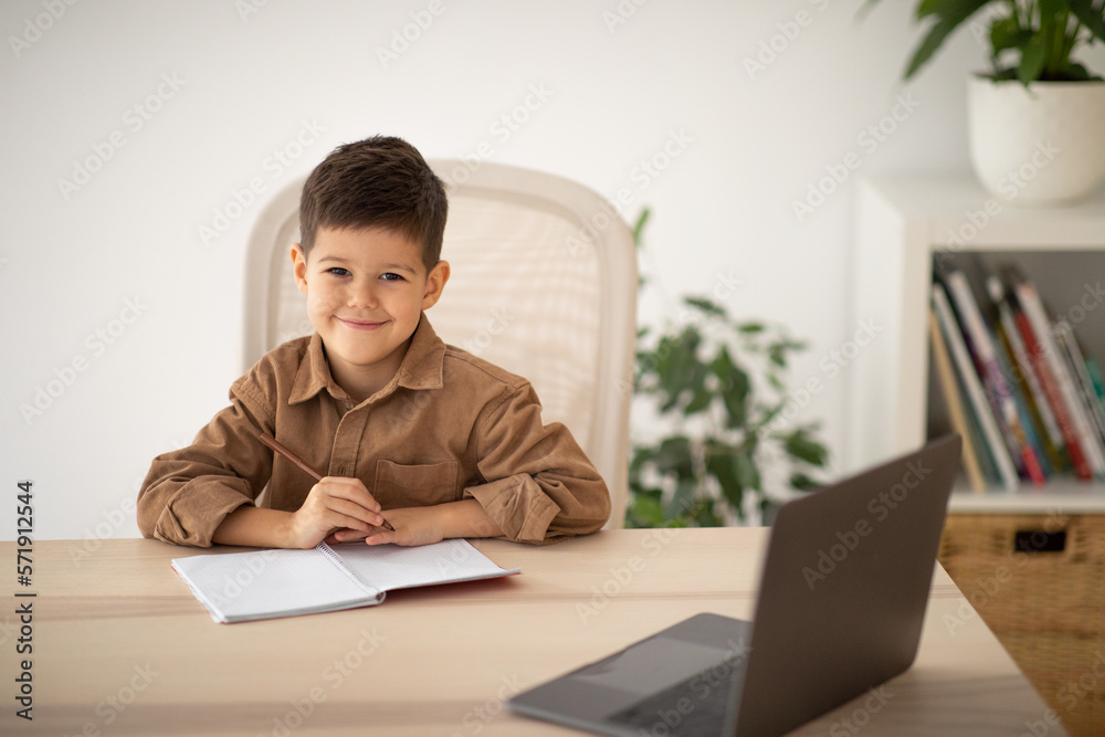 Cheerful european small kid has video call with teacher, tutor at table in elementary school, living room Cheerful european small kid has video call with teacher, tutor at table in elementary school, living room