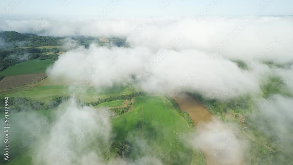 Flying above the clouds over beautiful green fields and a river seen through holes in the clouds. Aerial. 4K. 