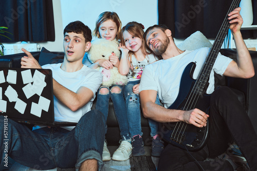 Staged photo. Homosexual couple and their children at home. The whole family gathered on the couch. Shall we try out our new guitar? There is a special program for tuning musical instruments.