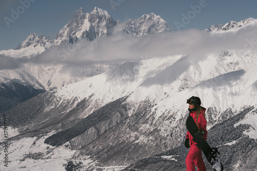 Snowboarder female walking with snowboard in beautiful mountains tops covered with snow and clouds on background