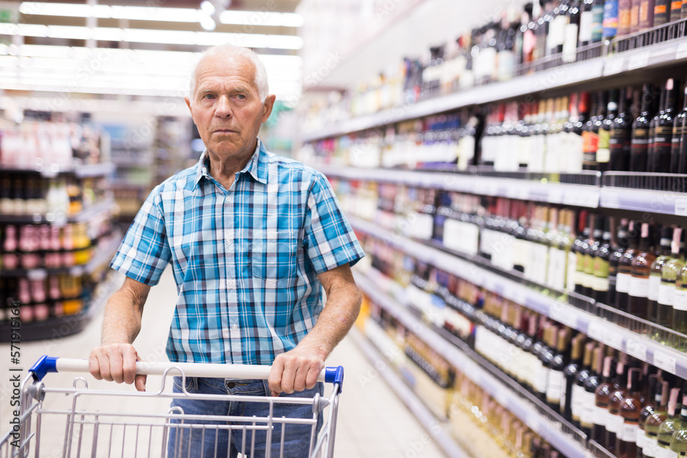 mature senor choosing alcoholic drinks in supermarket