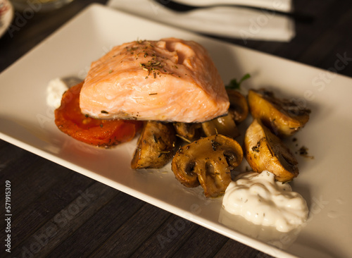 steamed salmon fillet on a pillow of fried mushrooms and tomatoes on a white plate