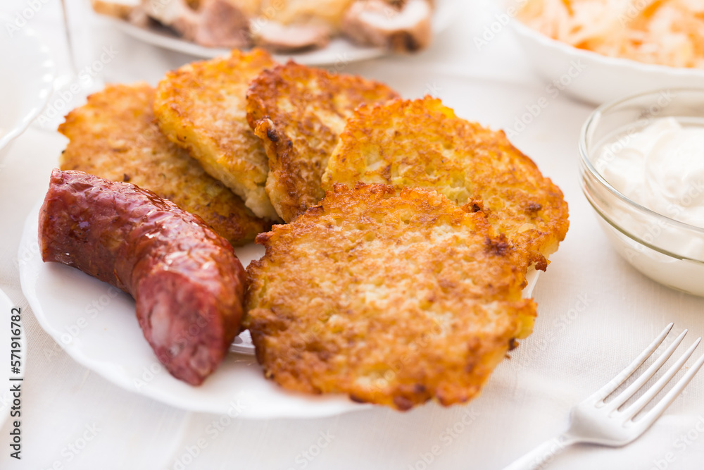 Fried grated potato pancakes with fried sausage on white plate Fried grated potato pancakes with fried sausage on white plate