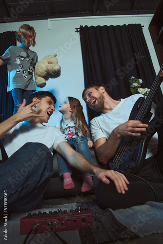 Staged photo. Homosexual couple and their children at home. The whole family gathered on the couch. Home concert with a guitar. One of the girls sings with her toy bear. Great party!