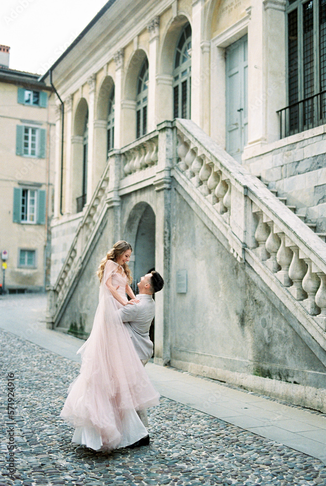 Groom lifts bride in his arms on the paving stones near the old building. Bergamo, Italy