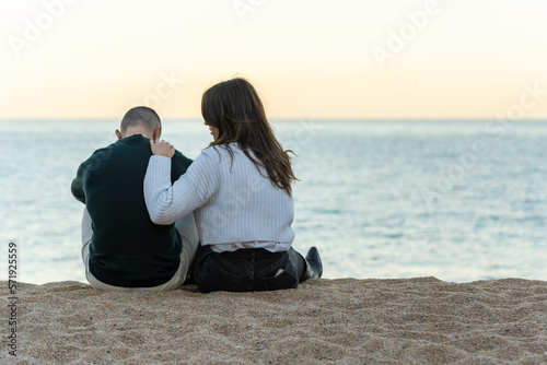 Woman consoling her friend while sitting on the sand at the beach